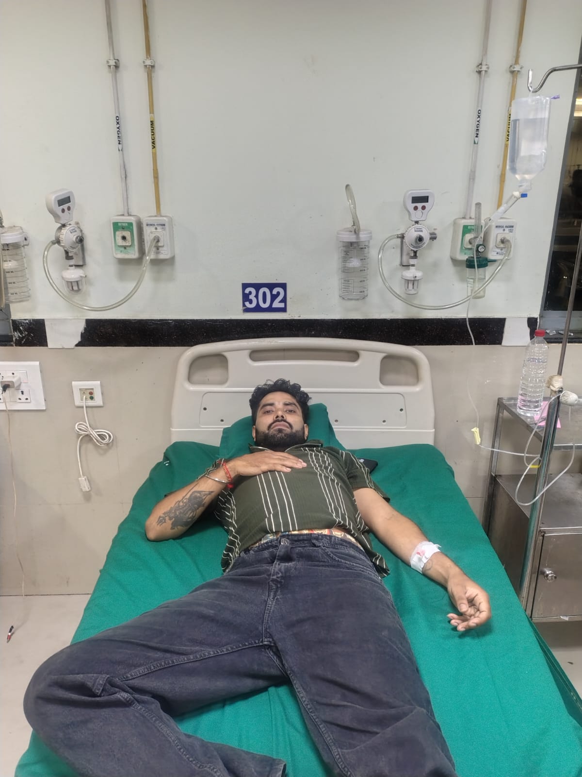Sumit Sarkar lying on a hospital bed at GMCH Guwahati, with an IV line attached